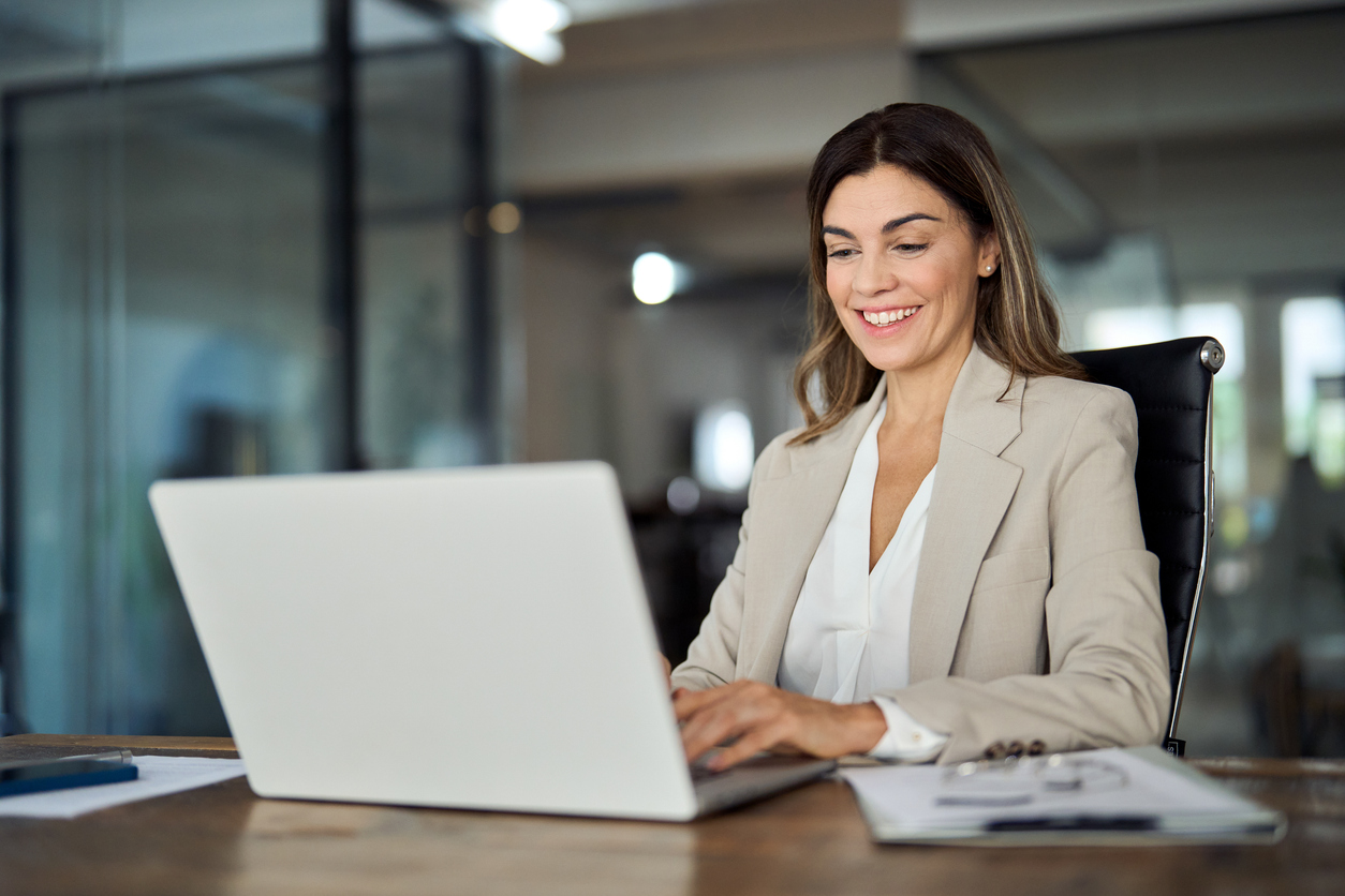 Happy mature business woman entrepreneur in office using laptop at work, smiling professional middle aged 40 years old female company executive wearing suit working on computer at workplace.