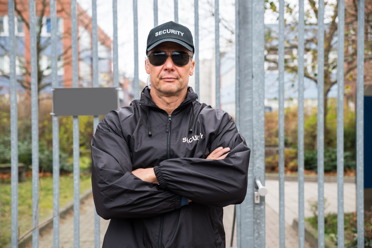 Portrait of confident mature security guard standing arms crossed in front of gate