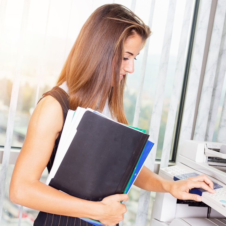 Smiling female assistant using copy machine in modern office